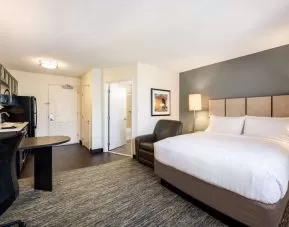 Double bed guest room in Sonesta Simply Suites Plano Frisco, furnished with kitchen, art on the wall, and an armchair.