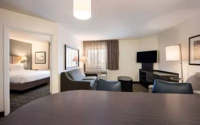 Sonesta Simply Suites Dallas Las Colinas double bed guest room, including sofa, window, and TV.