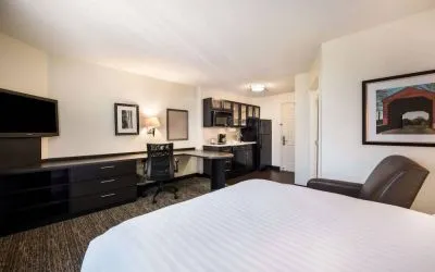Sonesta Simply Suites Dallas Las Colinas double bed guest room, furnished with armchair, TV, and workspace desk and chair.