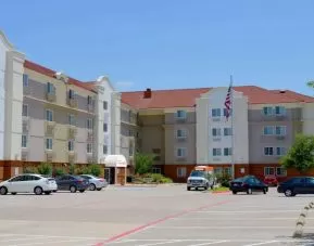 The hotel’s exterior has ample parking for guests, a US flag fluttering on a flagpole, and abundant greenery.