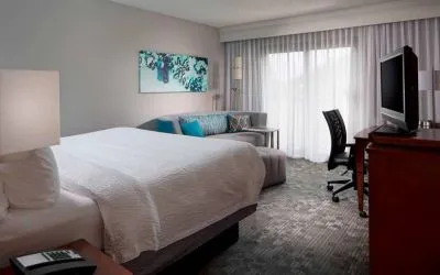 Sonesta Select Boca Raton double bed guest room, including sofa, window, TV, and a workspace desk and chair.