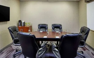 Hotel meeting room, with a wooden table surrounded by six leather chairs, a wall-mounted TV, and a whiteboard.