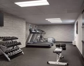 The fitness center at Sonesta Select Phoenix Camelback is equipped with free weights, a range of exercise machines, and a wall-mounted television.
