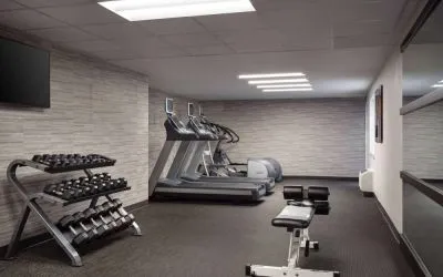 The fitness center at Sonesta Select Phoenix Camelback is equipped with free weights, a range of exercise machines, and a wall-mounted television.