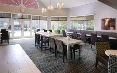 Sonesta ES Suites Dallas Medical Market Center’s lobby is furnished with a mix of table sizes and both regular and tall chairs, with plenty of natural light flowing through large windows.