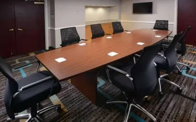 Hotel meeting room, with long wooden table, eight swivel chairs, and a wall-mounted television.