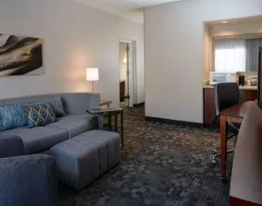 Guest room living area with sofa, chair, and TV at Sonesta Select Kansas City South Overland Park.