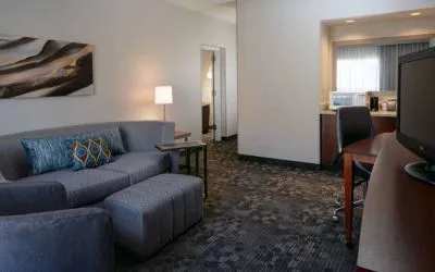 Guest room living area with sofa, chair, and TV at Sonesta Select Kansas City South Overland Park.