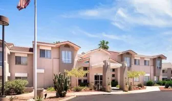 The hotel’s exterior has a fluttering USA flag flying from a flagpole and greenery including bushes, small trees, and a cactus.