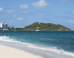 Waves coming on shore with view of resort buildings and mountainous island in distance. 