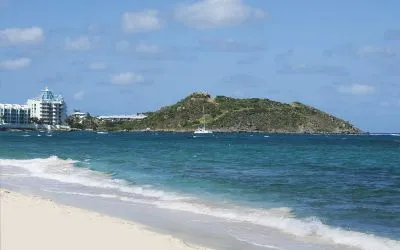 Waves coming on shore with view of resort buildings and mountainous island in distance. 