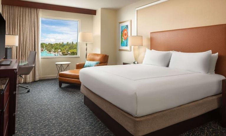 King room with TV, work desk, sofa and a great pool view at Hilton Orlando.