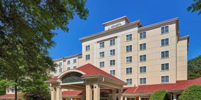 Sonesta Atlanta Airport South’s exterior features a covered entrance, well-kept greenery, and stylish red roof tiles.