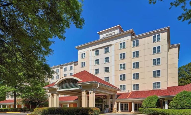 Sonesta Atlanta Airport South’s exterior features a covered entrance, well-kept greenery, and stylish red roof tiles.