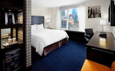 King bedroom with TV, work station and a view of the city at Hilton New York Fashion District.