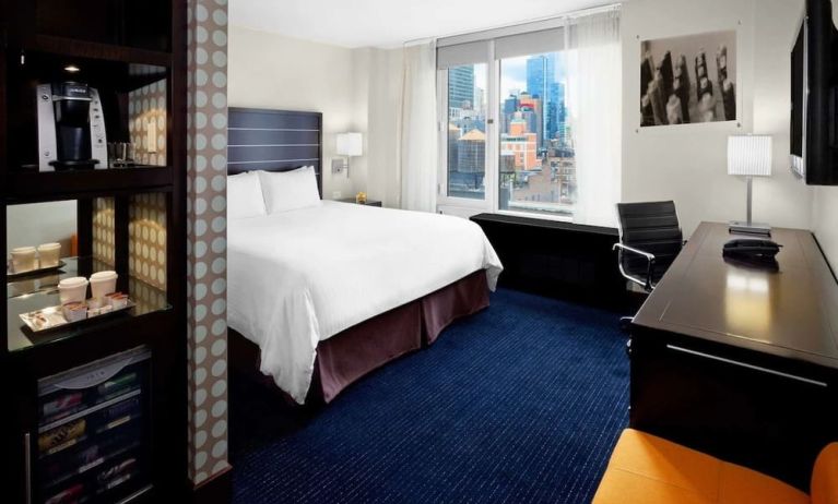 King bedroom with TV, work station and a view of the city at Hilton New York Fashion District.