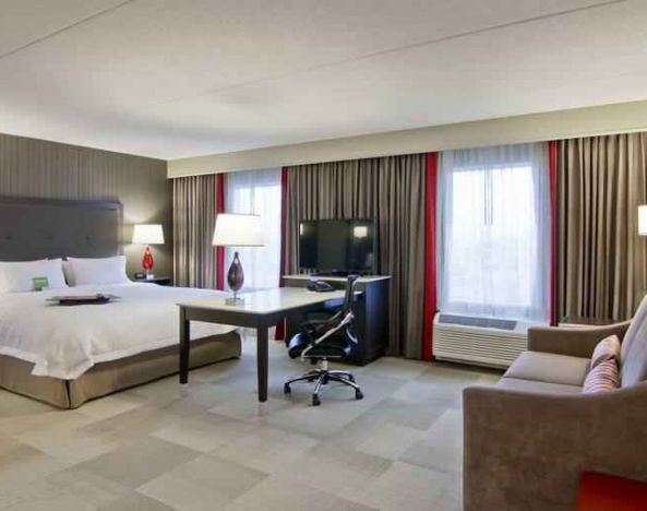 Hotel room with king size bed, sofa, TV and working station at the Hampton Inn & Suites by Hilton Toronto Markham.
