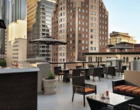 Elegant bar and a spacious rooftop filled with couches and small tables, skyline backdrop of downtown Los Angeles.