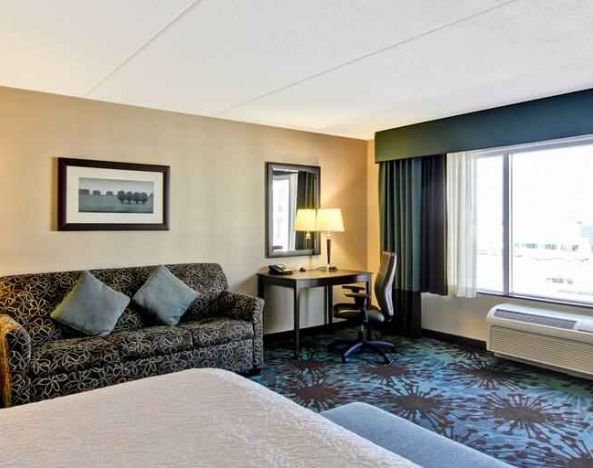 Hotel room with king size bed, living room and window view at the Hampton Inn by Hilton Toronto Airport Corporate Centre.