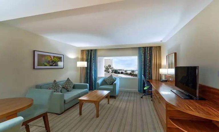 Spacious living area with TV screen, desk and sofa in a king room at the Hilton Ras Al Khaimah Beach Resort.