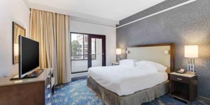 King size bed, large window and TV screen in a king room at the Embassy Suites by Hilton Alexandria-Old Town.