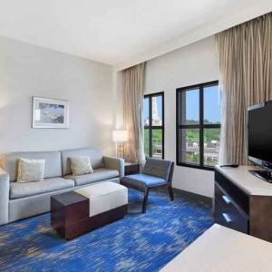 Spacious living room with desk, sofa, TV screen and windows at the Embassy Suites by Hilton Alexandria-Old Town.