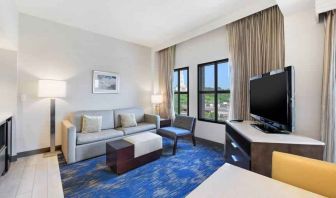 Spacious living room with desk, sofa, TV screen and windows at the Embassy Suites by Hilton Alexandria-Old Town.