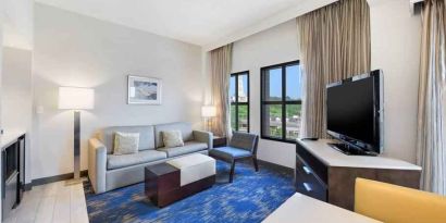 Spacious living room with desk, sofa, TV screen and windows at the Embassy Suites by Hilton Alexandria-Old Town.