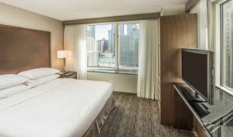 King size bed, TV screen and large window in a bedroom at the Embassy Suites by Hilton Chicago Magnificent Mile.