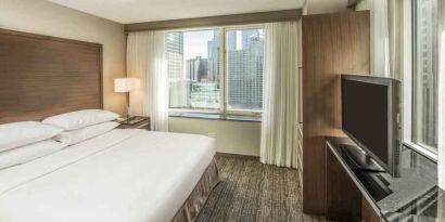 King size bed, TV screen and large window in a bedroom at the Embassy Suites by Hilton Chicago Magnificent Mile.