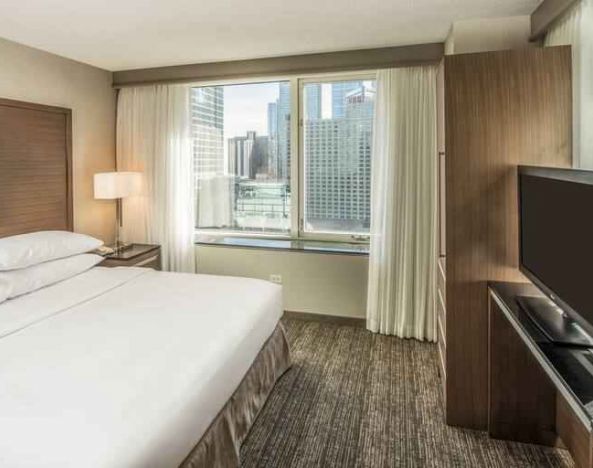 King size bed, TV screen and large window in a bedroom at the Embassy Suites by Hilton Chicago Magnificent Mile.