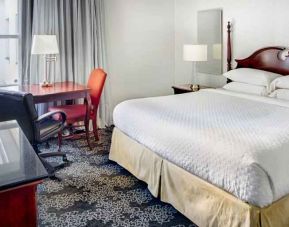 King size bed, desk and TV screen in a hotel room at the Embassy Suites by Hilton Portland-Downtown.