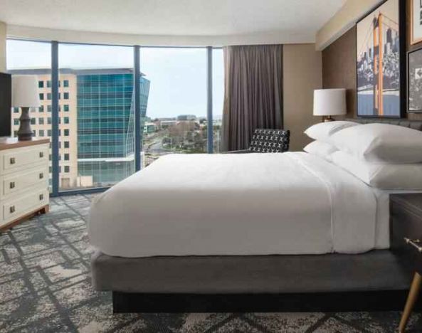 King size bed, TV screen and large window in a hotel room at the Embassy Suites by Hilton San Francisco Airport.