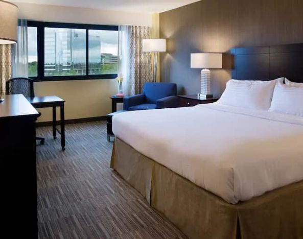 Spacious king size room with a king bed, chair. desk and view of city at the Hilton Nashville Airport.