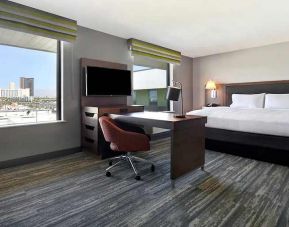 spacious king bedroom with work desk, large windows, natural light, and city views at Hampton Inn & Suites Las Vegas Convention Center.