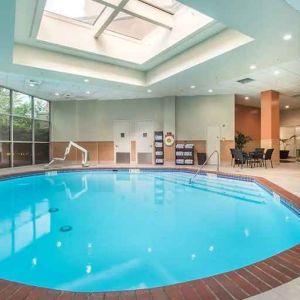 Bright-lit indoor pool with sun roof and comfortable seating area at Embassy Suites by Hilton Seattle Tacoma International Airport.