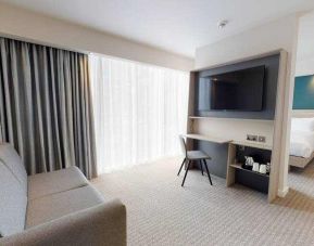 Living room with sofa, TV screen and desk at the Hampton by Hilton Manchester Northern Quarter.