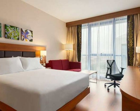 comfortable king bed with work desk, TV, and large windows at Hilton Garden Inn Sevilla.