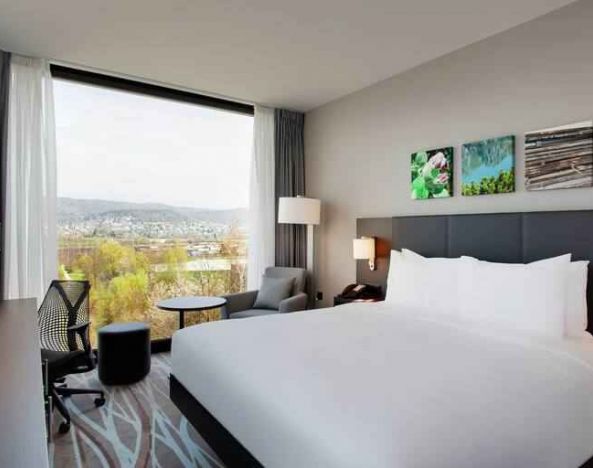 Bright king bedroom with desk along the window at the Hilton Garden Inn Zurich Limmattal.