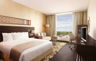 Spacious executive day room with floor-to-ceiling window, large desk, television, king bed at the Hilton Jaipur.