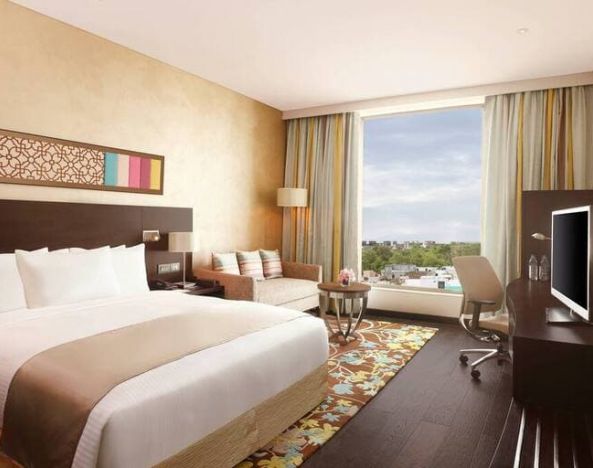 Spacious executive day room with floor-to-ceiling window, large desk, television, king bed at the Hilton Jaipur.