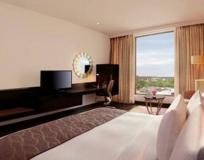 Bright king guest room with view out into Jaipur, India, complete with sitting area and long desk with television and workspace.