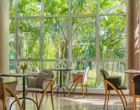Large windows surrounded by foliage with small circular tables to eat, work, socialize.