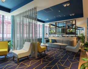 Stylish muted gold and pale blue lounge chairs along with a couch complement a blue and white geometric rug in the Antwerp Hilton lobby.