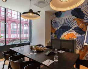 Floral artistic wall pattern and large window view of Antwerp complements a dark brown wooden table and place settings for 8 people to meet and do business in.