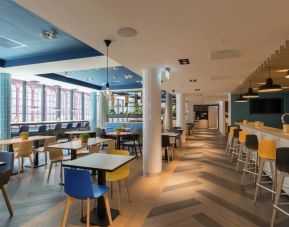 Large lobby with tall ceiling and floor to ceiling window view of downtown Antwerp, various types of seating for socializing, working, eating.