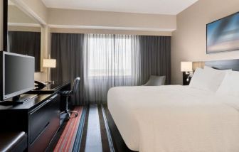 Spacious delux king room with TV, business desk, and couch at Courtyard By Marriott New York JFK Airport.