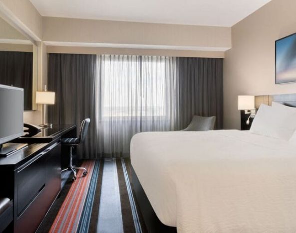 Spacious delux king room with TV, business desk, and couch at Courtyard By Marriott New York JFK Airport.