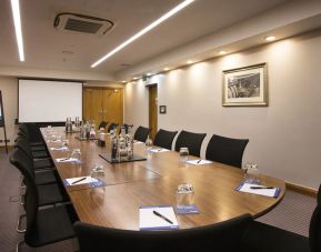 A wider shot of the meeting room with over half a dozen chairs, multiple tables, and a screen.