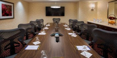 Meeting room in the Hilton Garden Inn Chicago Downtown Riverwalk, with long table, surrounding chairs and large TV.